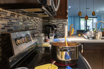 a shiny pot with a wooden spoon over the electric stove in the kitchen. View of the kitchen and dining room at the background