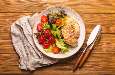 Healthy green vegetable salad with grilled chicken breast fillet on ceramic plate on rustic wooden kitchen table top view flat lay, diet food and clean eating concept 
