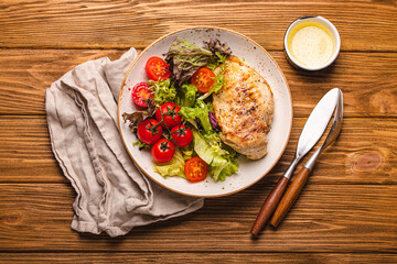 Healthy green vegetable salad with grilled chicken breast fillet on ceramic plate on rustic wooden kitchen table top view flat lay, diet food and clean eating concept 
