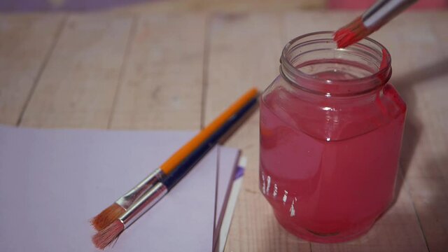 Artist washing paint brush in jar of water 