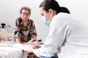 middle-aged latin male physician writing prescription at home for middle-aged woman