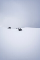 Traditionelle Almhütte aus Holz in kalter verschneiter Winternatur auf einer Alpe in den bayerischen Alpen an einem stürmischen Schneetag