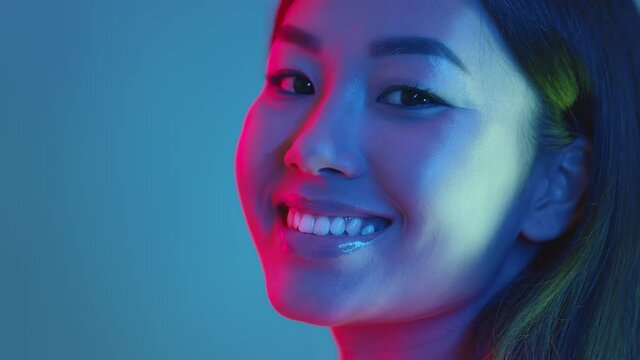 Trendy beauty. Young positive asian woman turning face to camera and smiling, bright neon lights, empty space