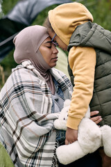 Young refugee female and her little daughter with toy touching by their foreheads