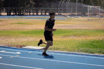 Man jogging on a blue running track, wearing black sports wear