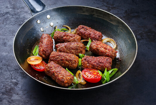 Traditionelle kroatische Cevapi als w&uuml;rzige Fleischb&auml;llchen mit Tomaten und Zwiebelringen, serviert als close-up in einer Bratpfanne 