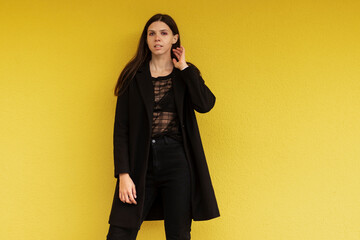 Portrait of a young stylish woman in black clothing. Against the background of a yellow wall.