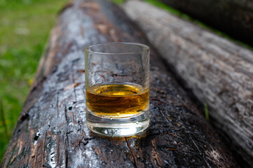 Glass of strong scotch single malt whisky on old log soaked in creosote