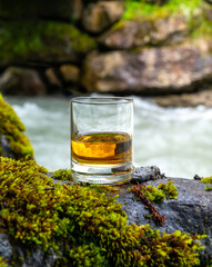 Glass of strong scotch single malt whisky with fast flowing mountain river on background