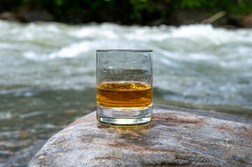 Glass of strong scotch single malt whisky with fast flowing mountain river on background