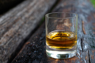 Glass of strong scotch single malt whisky on old log soaked in creosote