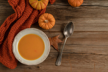bowl of pumpkin soup on the wooden table decorated with winter squash and autumn leaves
