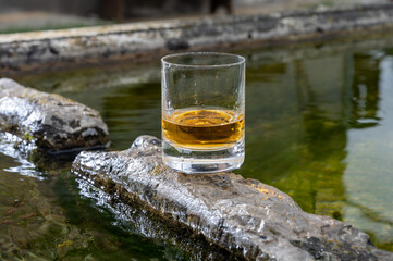 Glass of strong scotch single malt whisky served on old stone reservoir for water from mountain spring