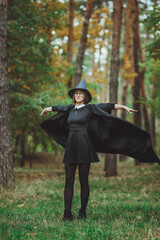Halloween Witch. Portrait of a girl in a hat and a witch costume in the forest. Ready for trick or treat holiday
