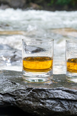 Glass of strong scotch single malt whisky with fast flowing mountain river on background