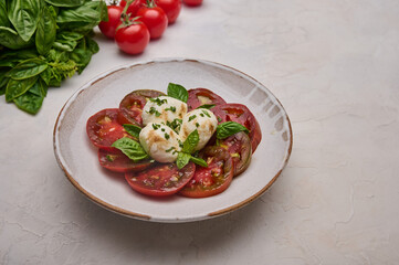Delicious caprese salad with red tomatoes, fresh basil and mozzarella cheese in white plate. Close up 