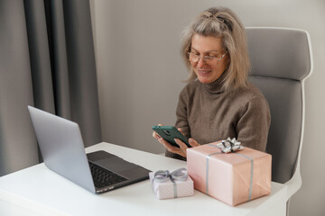 A middle aged woman makes order and purchases of christmas gifts by smartphone