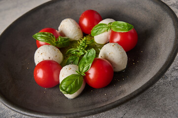 Macro italian caprese salad with ripe tomatoes, fresh basil and mozzarella cheese in black plate