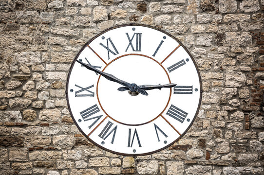 Wall clock antique vintage on a stone wall of a tower with Roman numerals, large antique clock