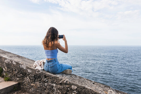 young female traveler taking photos of the ocean with her smartphone