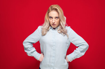 Impatient young woman with hands on waist looking to camera, isolated on red background. Angry girl - obrazy, fototapety, plakaty