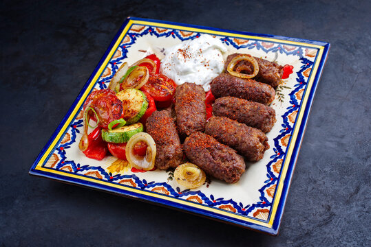 Traditional Croatian cevapi spicy meat ball rolls with BBQ vegetable and tzatziki served as top view on a rustic plate