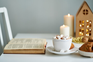 Reading book on cozy winter evening with candles, cocoa hot chocolate with marshmallows and...