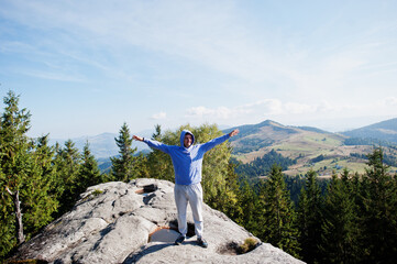 Happy hiker with hands in the air stand on rock. View over rocky valley.