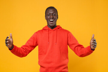 Excited young african american man in red streetwear hoodie posing isolated on yellow background. People lifestyle concept. Mock up copy space. Gesturing demonstrating size with horizontal workspace.