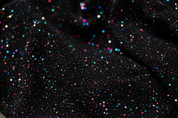 black crumpled fabric with multicolored sequins as background, shiny fabric