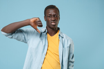 Fototapeta premium Dissatisfied young african american man guy in casual shirt, yellow t-shirt posing isolated on blue wall background studio portrait. People lifestyle concept. Mock up copy space. Showing thumb down.