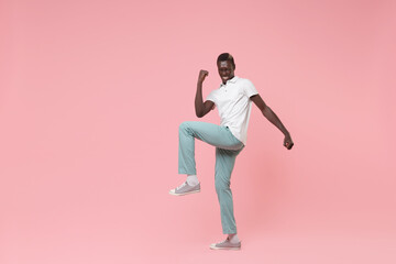 Fototapeta na wymiar Joyful young african american man guy in white polo shirt, turquoise trousers posing isolated on pastel pink background in studio. People lifestyle concept. Mock up copy space. Doing winner gesture.