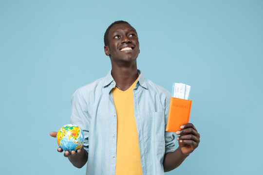 Smiling young african american man guy in casual shirt yellow t-shirt isolated on blue background. People lifestyle concept. Mock up copy space. Hold passport tickets Earth world glode looking up.