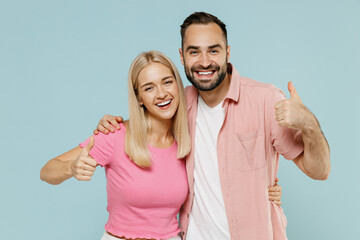 Young couple two friends family man woman in casual clothes looking camera together show thumb up gesture isolated on pastel plain light blue color background studio portrait People lifestyle concept.
