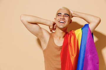 Young laughing minded happy blond latin gay man with make up in beige tank shirt with rainbow flag...