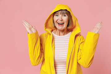 Joyful mature elderly woman 55 years old wears yellow waterproof raincoat hood spreading hands...