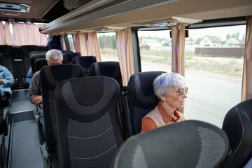Aged Caucasian woman with grey hair sitting by window inside bus and looking at road and country...