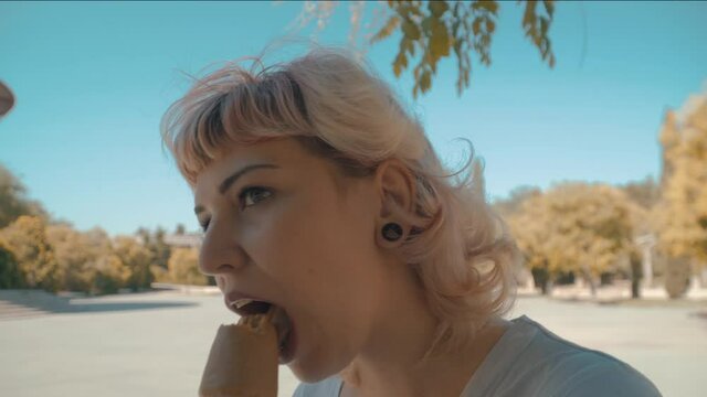Mujer de pelo rubio con una dilatación en la oreja comiéndose un helado, chica joven comiendo un helado de adoquín ,mujer de pelo corto chupando un helado de chocolate