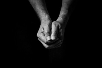 Male hands held out, clasped together in thought or prayer.