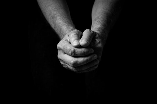 Male hands held out, clasped together in thought or prayer.