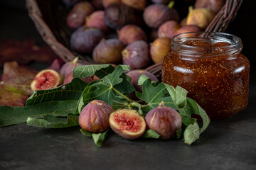a basket of fresh figs and a jar of fig jam on a dark gray background
