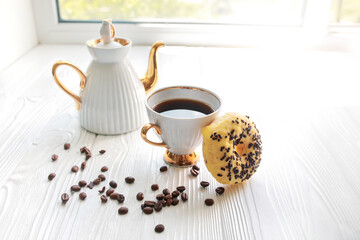 white porcelain teapot and cup on white wooden table on windowsill on sunny day. Tea after game. Chess pieces near coffee beans. Chess player's breakfast