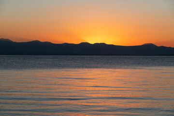 
Beautiful bright sunset sky on the lake and silhouette mountains on the horizon.