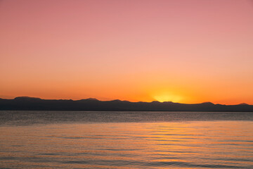 Fototapeta premium Beautiful bright sunset sky on the lake and silhouette mountains on the horizon.