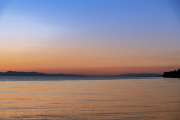 Fototapeta premium Beautiful bright sunset sky on the lake and silhouette mountains on the horizon.