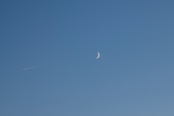 New moon and plane on the blue sky.