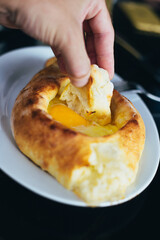 Man eating khachapuri dipping a piece of baked dough into a raw egg - the national georgian food of the caucasus