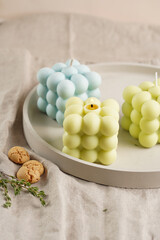 Green, blue and white square bubble candles on a concrete tray on a linen table cloth