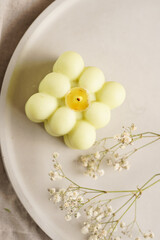 One white square bubble candle on a concrete tray on a linen table cloth with a blooming branch, top view