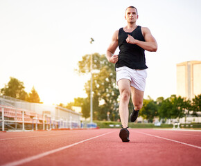 Young muscular fit male sprinter running on a red running track - Fitness and wellness concept with a millennial runner - Copyspace on the photo's left side